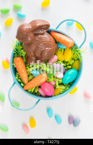 Easter basket with chocolate rabbit, candy eggs, and mini carrots on white background with jellybeans Stock Photo