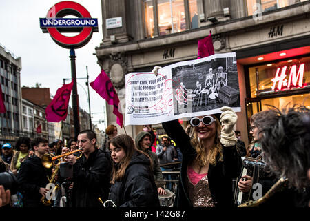 London, UK. 12th Apr, 2019. A woman activist seen holding a banner during the event. The Extinction Rebellion Fashion Action group brought Oxford Circus to a standstill by staging a creative and symbolic catwalk titled Fashion: Circus of Excess. The objective is to raise the alarm about the role fashion consumption plays in fuelling the Climate and Ecological emergency. The fashion industry is set to consume a quarter of the world's carbon budget by 2050 in clothing production. Credit: SOPA Images Limited/Alamy Live News Stock Photo