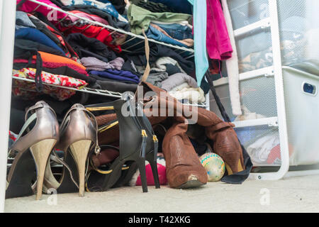 Woman's closet with high heel shoes, stacked, folded clothes on shelves and part of robes hanging. Depicting closet organization, donating clothes. Stock Photo