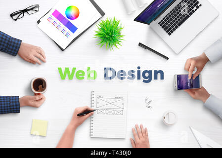 Web design text on work desk surrounded with web development team, devices, projects, and ideas on paper. Concept of team meeting. Stock Photo
