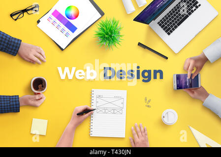 Web design team work on project concept. Yellow desk with web design text. Top view, flat lay. Stock Photo