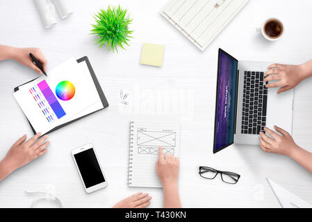 Top view scene of web design team work desk. Laptop computer with flat design web site concept, idea sketch on paper, color palette, cup of coffee, pl Stock Photo