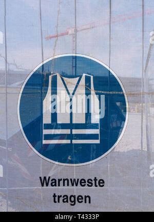 Symbol on a transparent tarpaulin as an indication of safety on a construction site. You can see that you should wear a safety vest. The text means in Stock Photo