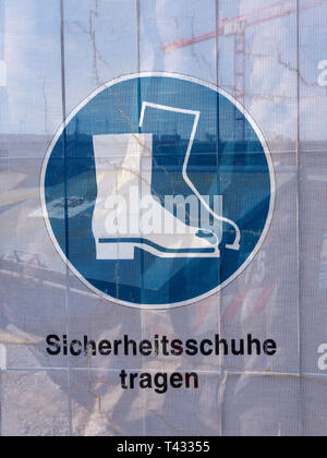 Symbol on a transparent tarpaulin as an indication of safety on a construction site. You can see that you should wear safety shoes. The text means in  Stock Photo