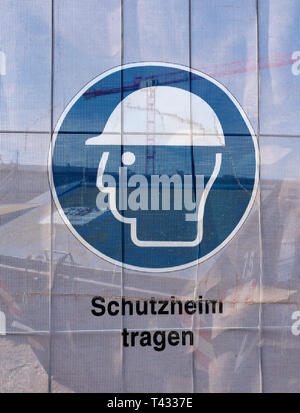 Symbol on a transparent tarpaulin as an indication of safety on a construction site. You can see that you should wear a hard hat. The text means in Ge Stock Photo