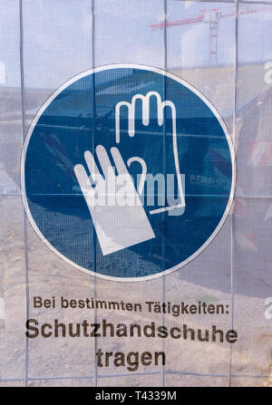 Symbol on a transparent tarpaulin as an indication of safety on a construction site. You can see that you should wear work gloves. The text means in G Stock Photo