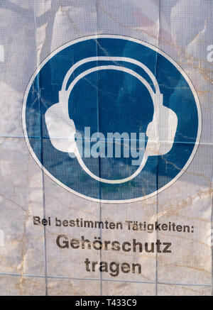 Symbol on a transparent tarpaulin as an indication of safety on a construction site. You can see that you should wear earmuffs. The text means in Germ Stock Photo