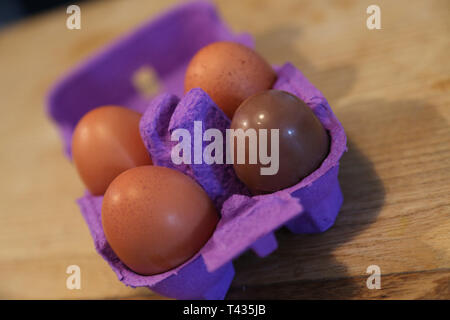 3 eggs and one chocolate egg on the pink cardboard on the wood table Stock Photo