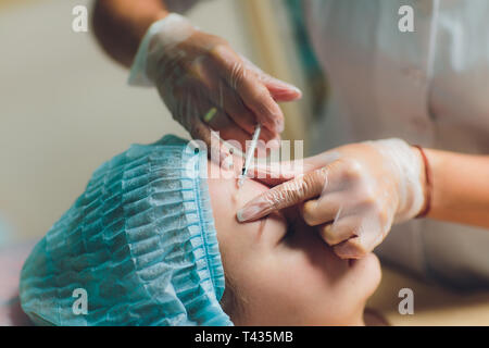 Doctor giving face lifting injection on mid age woman in the forehead between eyebrows to remove expression wrinkles in a clinic surgery room O.R Stock Photo