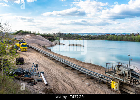 A string of transport belting in a gravel pit for transporting gravel and sand over long distances, belts go along the lake. Stock Photo
