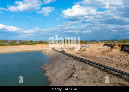 A string of transport belting in a gravel pit for transporting gravel and sand over long distances, belts go along the lake. Stock Photo