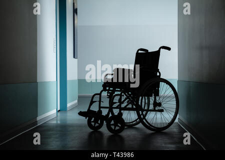 Silhouette Of Empty Wheelchair Parked In Hospital Corridor Stock Photo