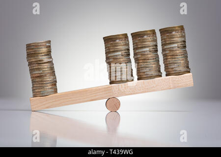 Stack Of Coins On Wooden Seesaw Over Gray Background Stock Photo