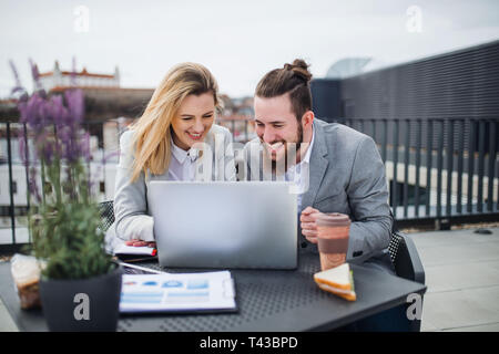 Two young business people with laptop sitting on a terrace outside office, working. Stock Photo