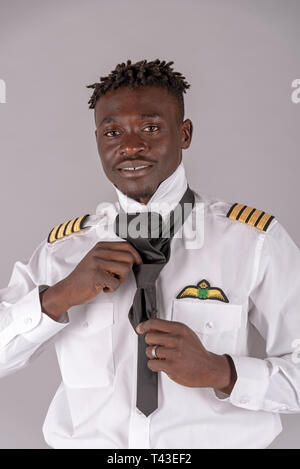 London,UK. April 2019.  A young airline pilot with an african dred hairstyle. Crew member tying his black tie, Stock Photo