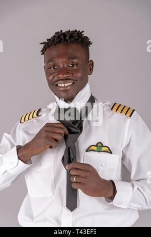 London,UK. April 2019.  A young airline pilot with an african dred hairstyle. Crew member tying his black tie, Stock Photo