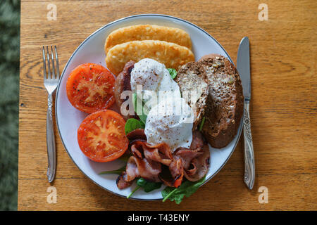 A cooked breakfast with bacon, eggs and hash browns served on a white plate Stock Photo