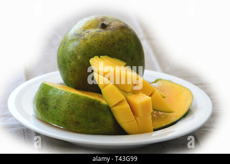 diced mango with whole fruit on side in white dish Stock Photo
