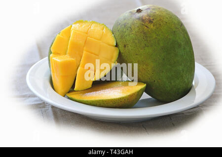 diced mango with whole fruit on side in white dish Stock Photo