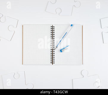 open notebook in a cell and a blue pen on a white background, next to large blank puzzles, top view Stock Photo