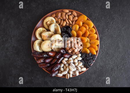 Dried Fruits and Nuts on platter, top view. Vegetarian healthy sweets on black, copy space. Stock Photo