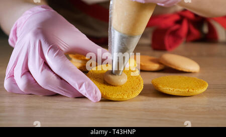 Pastry chef is filling cream lemon macaroons with pastry bag, close-up. Stock Photo