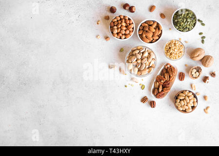 Various Nuts in  bowls on white background, top view, copy space. Pecans, hazelnuts, walnuts, pistachios, almonds, pine nuts, peanuts, pumpkin seeds. Stock Photo