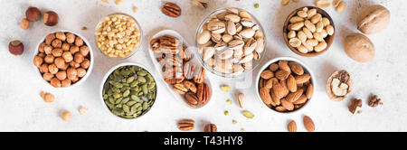 Various Nuts in  bowls on white background, top view, banner. Nuts assortment - pecans, hazelnuts, walnuts, pistachios, almonds, pine nuts, peanuts, p Stock Photo