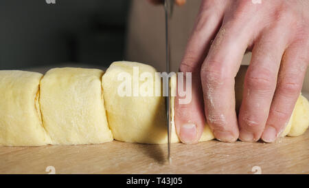Pastry chef cuts roll with cinnamon, sugar and butter on portions to bake cinnamon rolls. Hands close-up. Stock Photo