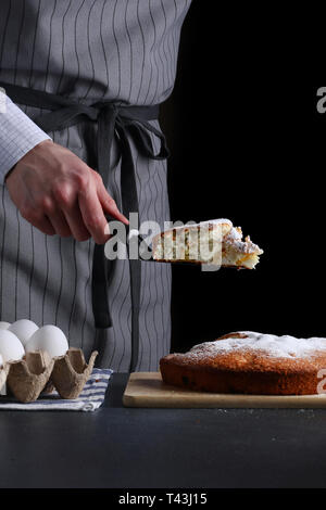 chef holding a piece of cake on black background. pie making and serve. Stock Photo