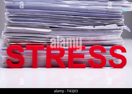 Close-up Of Red Stress Word Leaning On Documents On White Desk Stock Photo