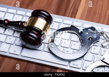 Close-up Of Gavel And Steel Handcuffs On White Keyboard Over Wooden Table Stock Photo