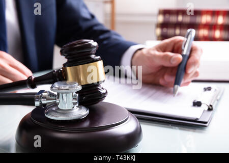 Judge Writing On Legal Documents With Mallet And Stethoscope Over Sound Block In Court Stock Photo