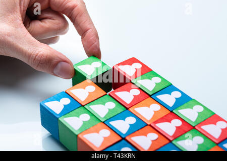 Businessperson's Hand Holding Green Cubic Block Near Team Of Red And Green Blocks Stock Photo