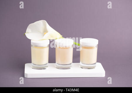 Luxurious cosmetic background. Candle Cream in three jars with white flower kala on grey background. Feminine skin care concept. Stock Photo