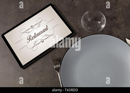 Tablet with stylish restaurant logo and laid table Stock Photo