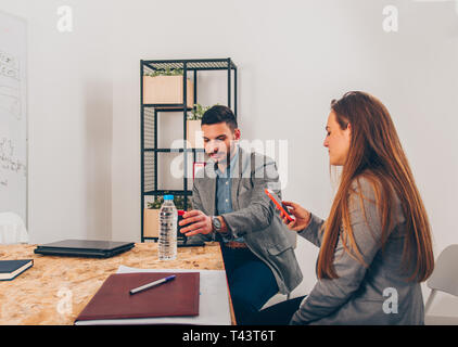 Business girl holding smartphone while sitting with her colleague Stock Photo