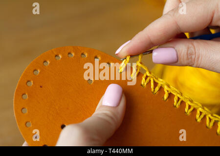 Hands of a young woman knit crochet from yellow yarn on a light wooden surface. Start a new bag of yarn. Selective soft focus. Stock Photo