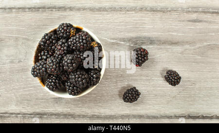 Top down view, small bowl with blueberries some of them spilled on desk. Stock Photo