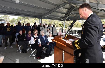 Panama City, FL -- Naval Support Activity Panama City commanding officer Cmdr. Jay Sego reads remarks during a ceremony honoring the service of a World War II Navy veteran, Thursday, Mar. 14, 2019.  Sego presented the Purple Heart and the Navy-Marine Corps Commendation Medal with Valor to Gunner's Mate 2nd Class Wheeler R. Ervin's daughter Nicole Ervin Parker, son-in-law Terry Parker, and grandson Kristopher Parker (front row, left-right) for Ervin's combat actions aboard the Liberty Ship SS William W. Gerhard in August 1943.  As a member of the Navy's Armed Guards whose mission was to protect Stock Photo