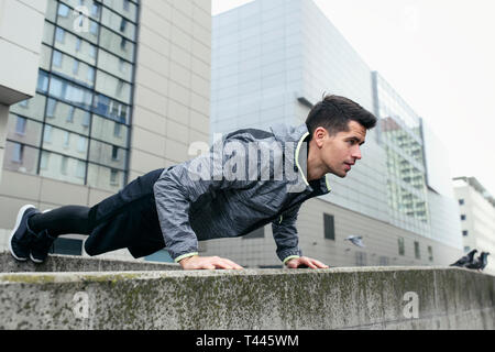 Portrait of sports man use architecture for his calisthenic workout. Push ups, in the background modern city buildings. Concept of healthy lifestyle. Stock Photo