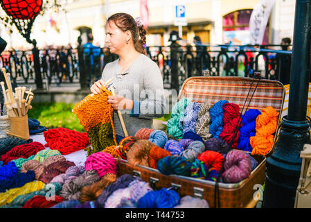Russia, city Moscow - September 6, 2014: Woman knits on the street. Women's hands knit a colorful product made of wool. Thick threads. Yarn sale on Stock Photo