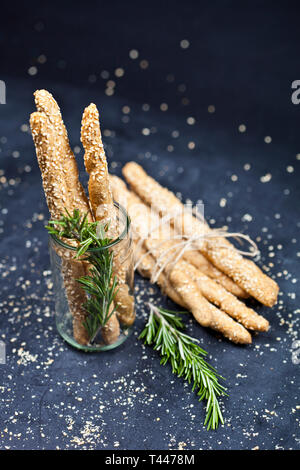 Italian grissini bread sticks with sesame and rosemary herb on black board background. Fresh italian snack. Stock Photo