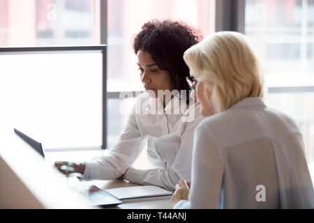 Serious diverse young and old businesswomen work together on laptop Stock Photo