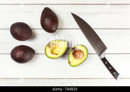 https://l450v.alamy.com/450v/t44b20/top-down-view-purple-brown-avocado-bilse-variety-on-white-wooden-desk-one-overripe-fruit-halved-pulp-parts-dark-chef-knife-next-to-it-t44b20.jpg