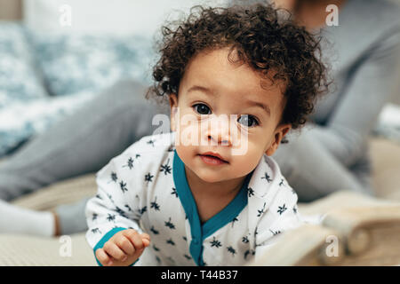 Close up portrait of a curly-haired baby boy crawling on bed Stock Photo