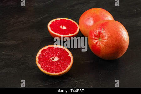 Pink grapefruits, one citrus fruit halved, on black slate board Stock Photo
