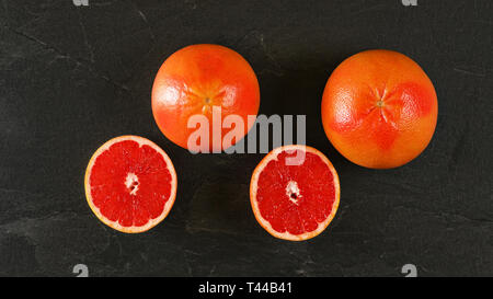 Flat lay photo - grapefruits, one halved, on black slate like board Stock Photo