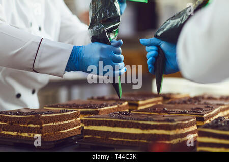 A confectioners decorates cream from a bag on a chocolate cake in a bakery. Stock Photo