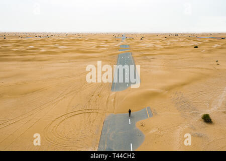View from above, stunning aerial view of an unidentified person walking on a deserted road covered by sand dunes in the middle of the Dubai desert.